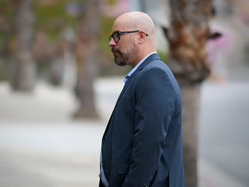 An agency partner in a navy blazer photographed in profile on a sunny palm-lined street