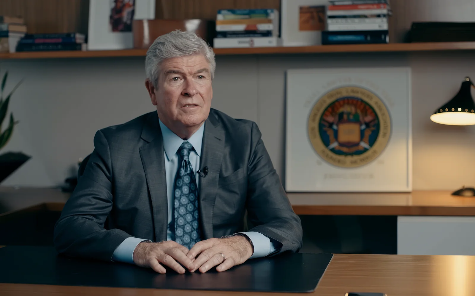Senior attorney seated for an attorney profile video with law office credentials behind him